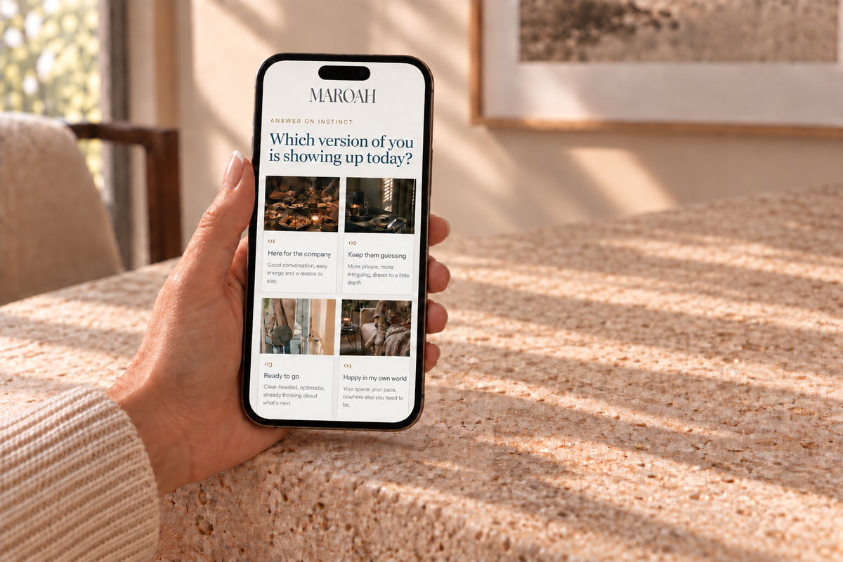 A hand holding a smartphone displaying the MAROAH website on a warm, sunlit stone tabletop.